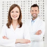 Team of two eye doctors, opticians or optometrists standing in optical shop.